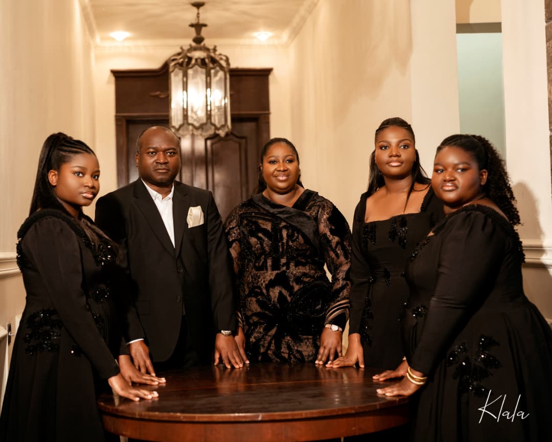 Dr AjokeSings with her husband and their three daughters, all in black, hands resting together on a wooden table